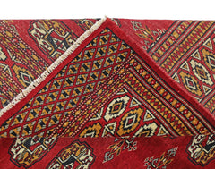 A vintage Pakistani Princess Bokhara rug featuring a red field with geometric patterns and a folded corner.