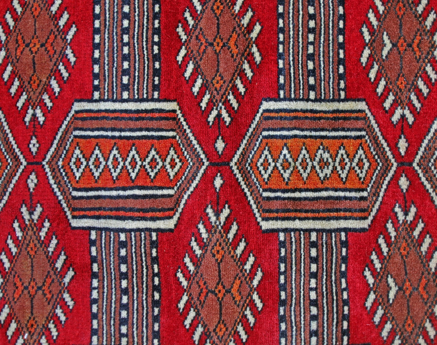 A vintage Pakistani Princess Bokhara rug featuring a repeating geometric pattern in red and orange.