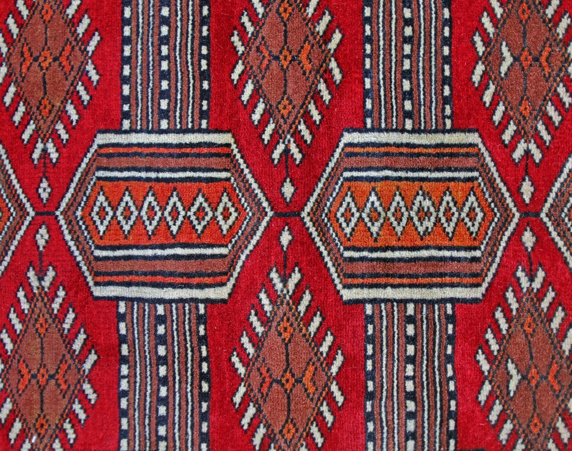 A vintage Pakistani Princess Bokhara rug featuring a repeating geometric pattern in red and orange.