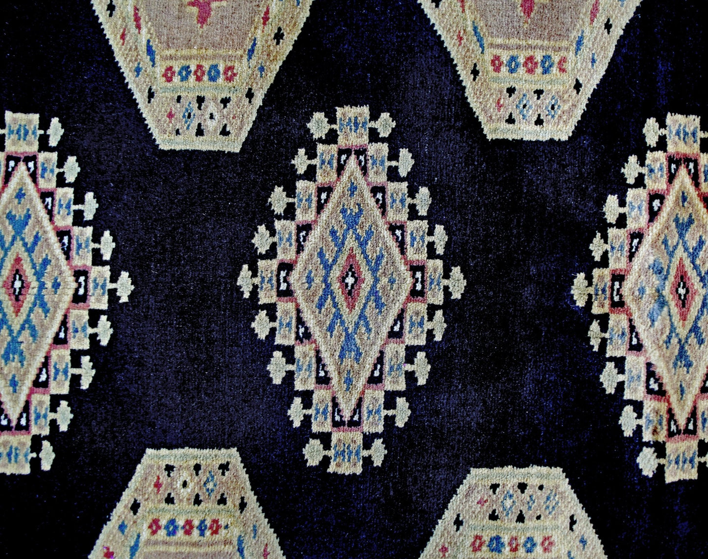 A vintage Pakistani Bokhara rug featuring a dark blue field with repeating geometric diamond motifs.