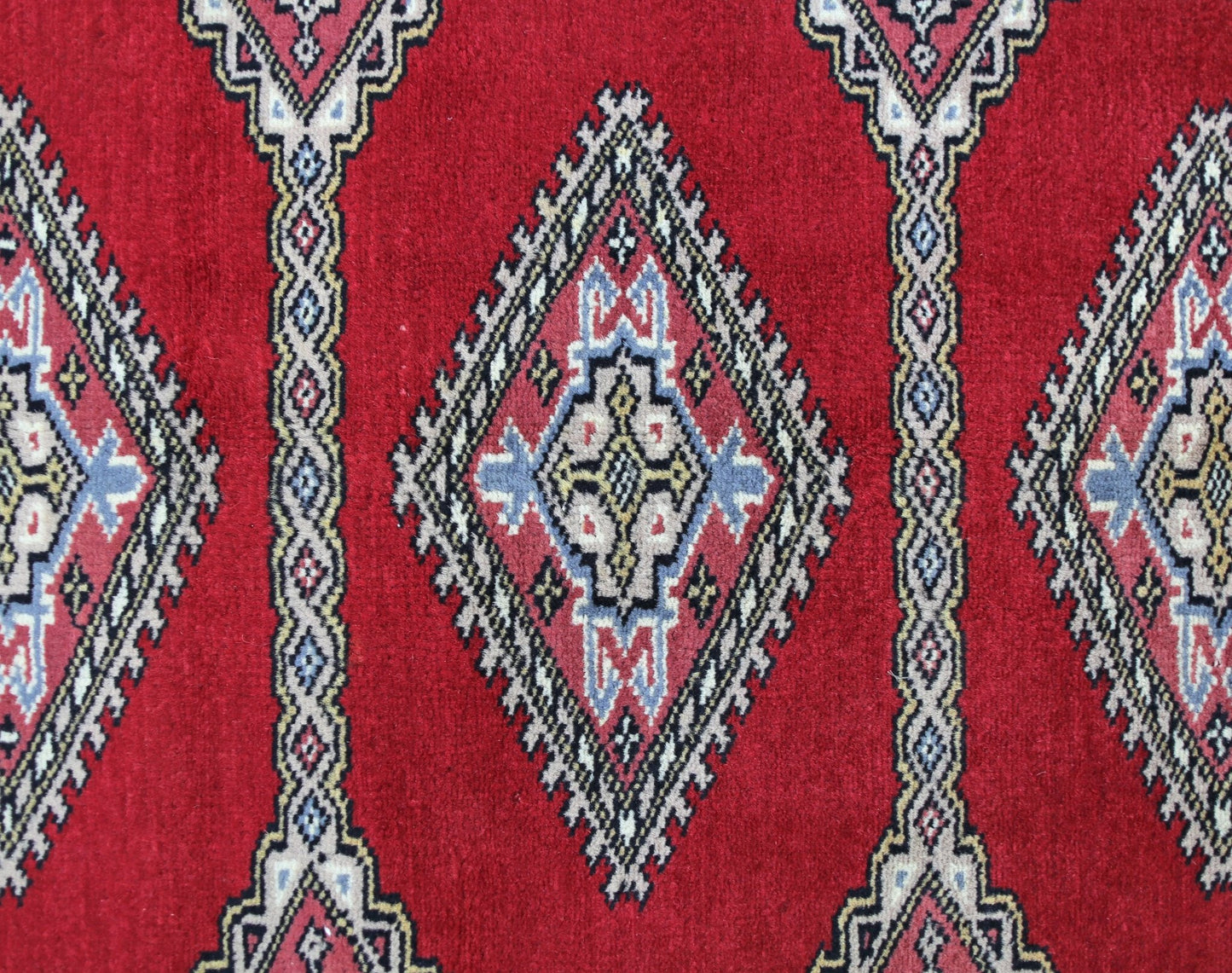 A vintage Pakistani Princess Bokhara rug featuring a repeating diamond pattern in red, blue, and cream.