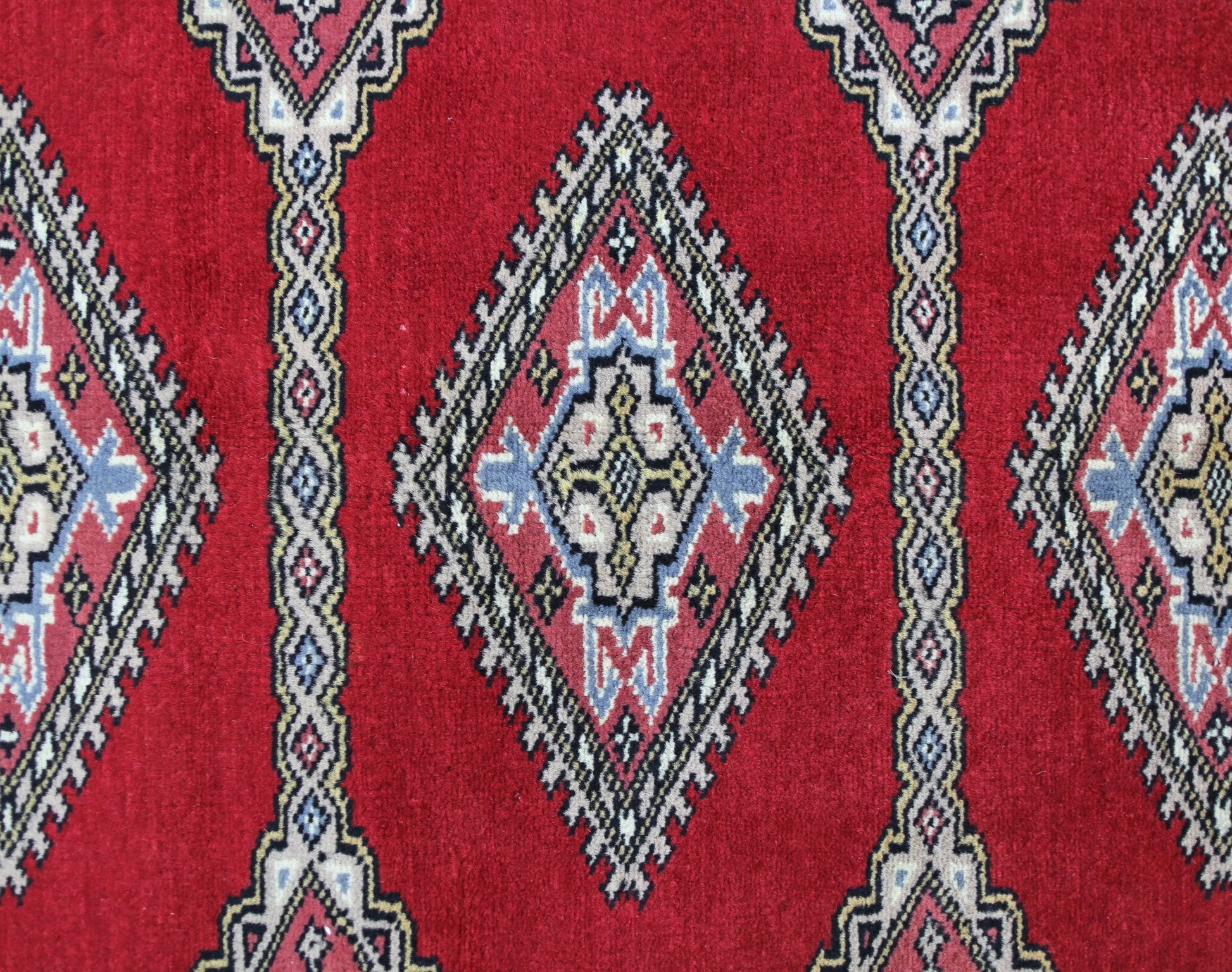 A vintage Pakistani Princess Bokhara rug featuring a repeating diamond pattern in red, blue, and cream.