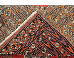 A folded vintage Pakistani Princess Bokhara rug featuring a geometric pattern in red and orange.