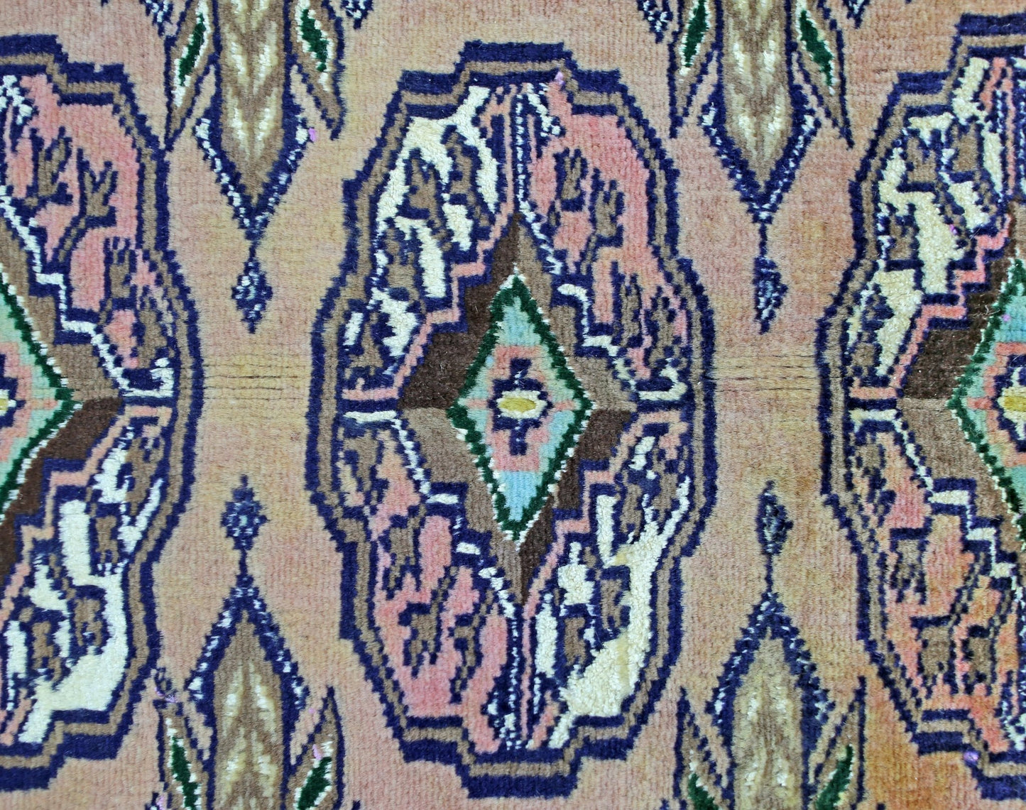 A vintage Pakistani Princess Bokhara rug featuring a repeating geometric medallion pattern in pink and blue.