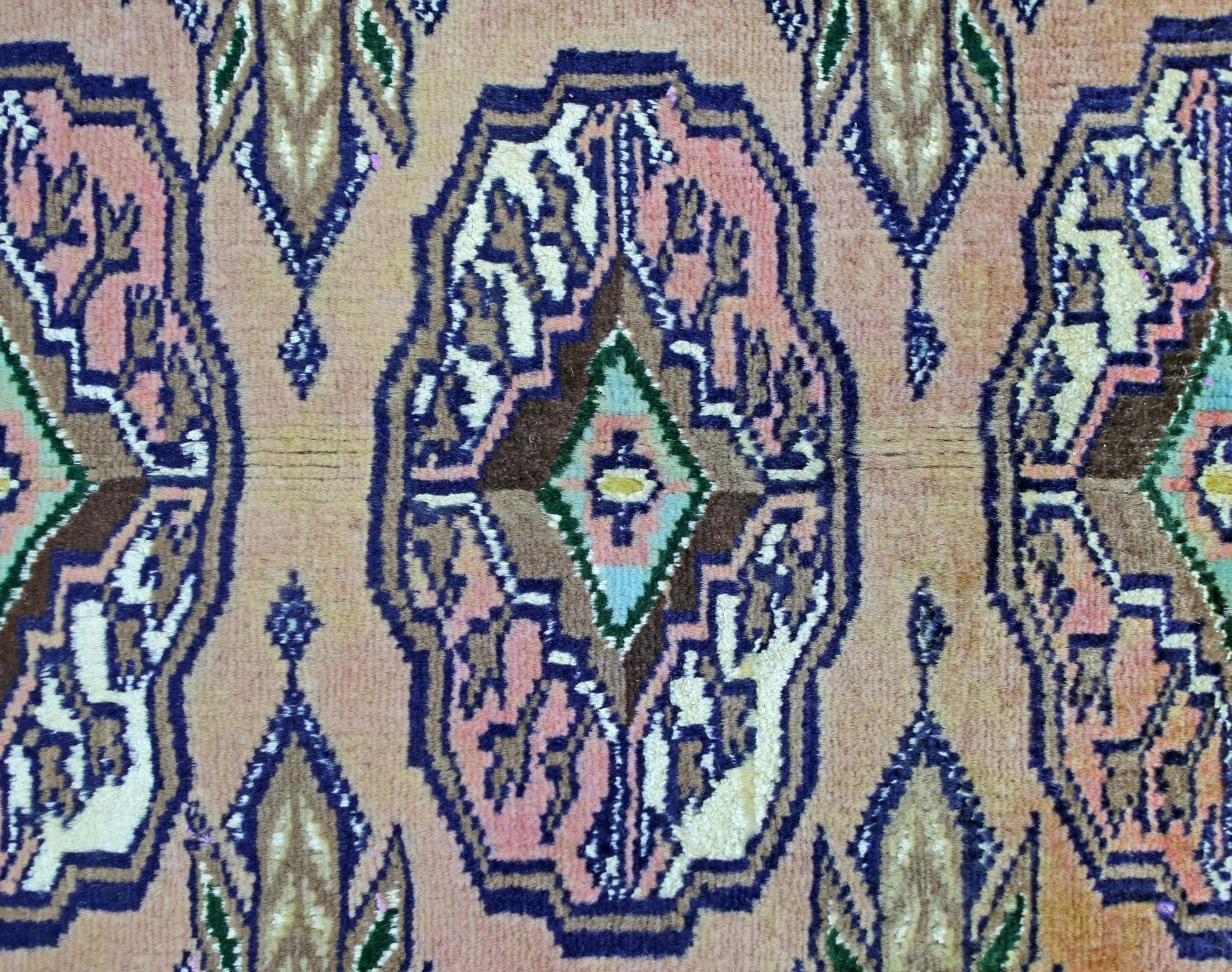 A vintage Pakistani Princess Bokhara rug featuring a repeating geometric medallion pattern in pink and blue.