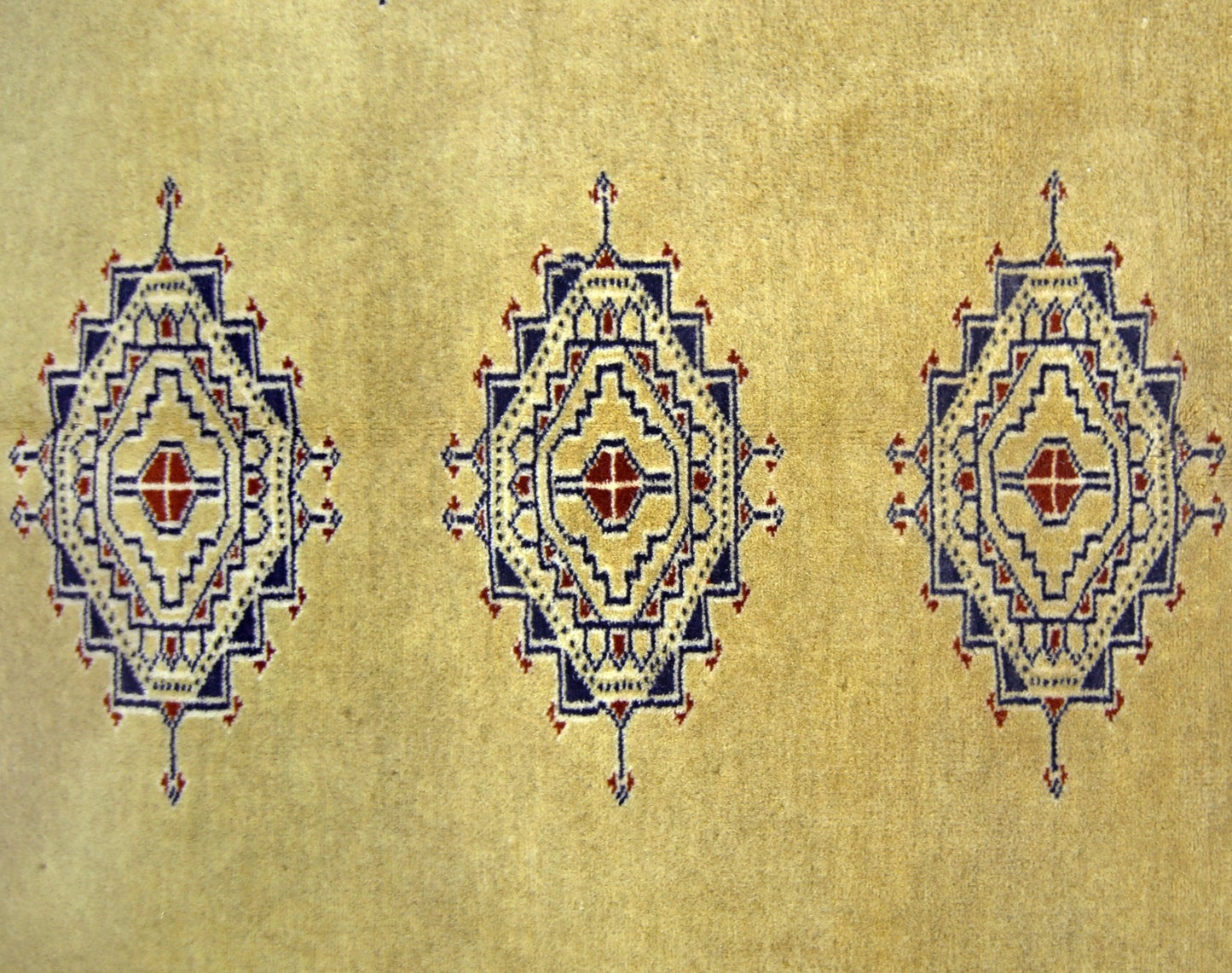 A vintage Pakistani Princess Bokhara rug featuring three repeating geometric medallions on a tan base.