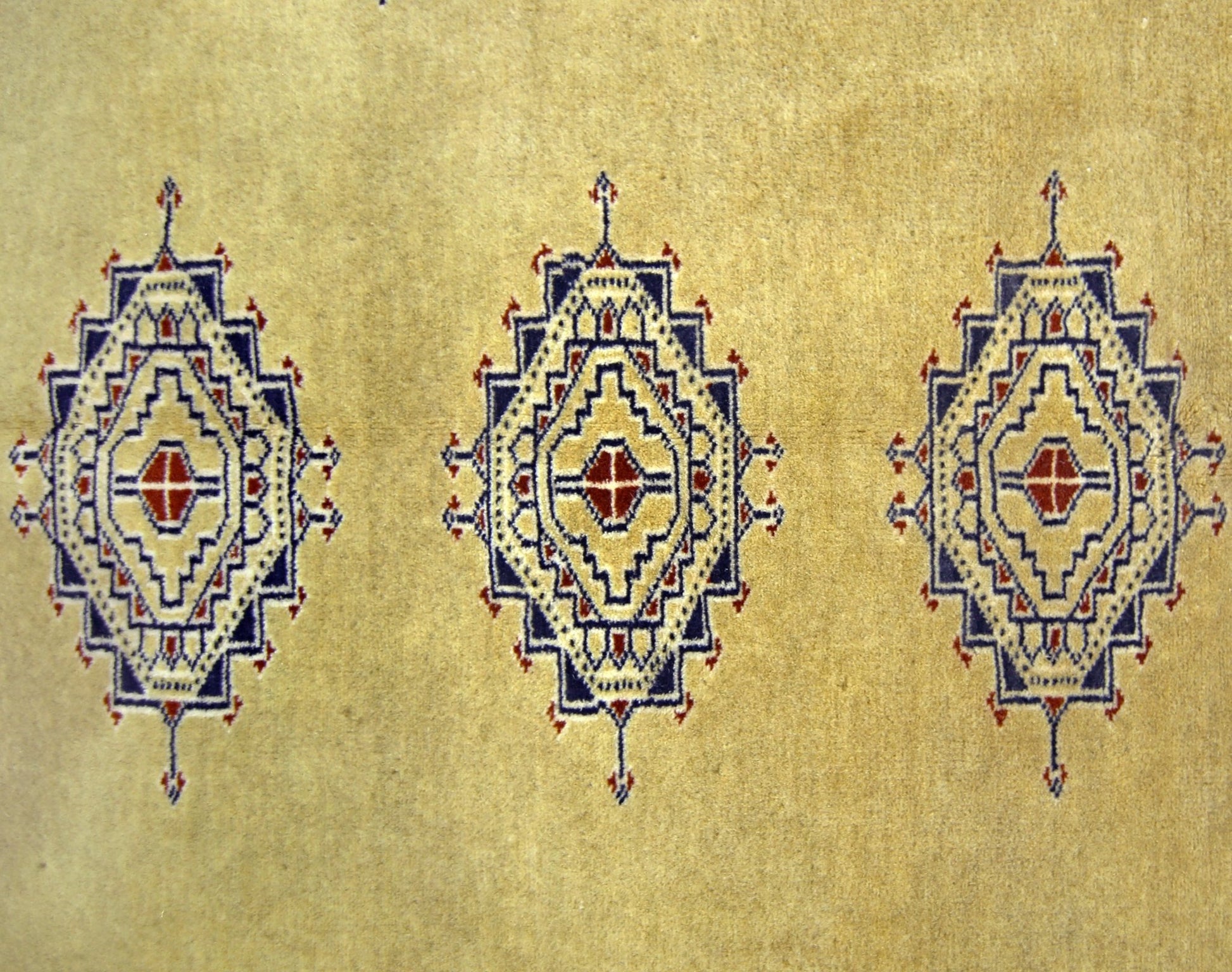 A vintage Pakistani Princess Bokhara rug featuring three repeating geometric medallions on a tan base.