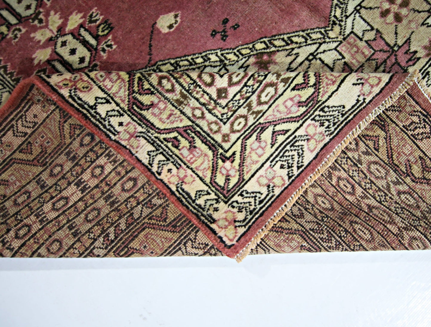 A vintage Pakistani Princess Bokhara rug with a folded corner revealing its intricate wool pattern.