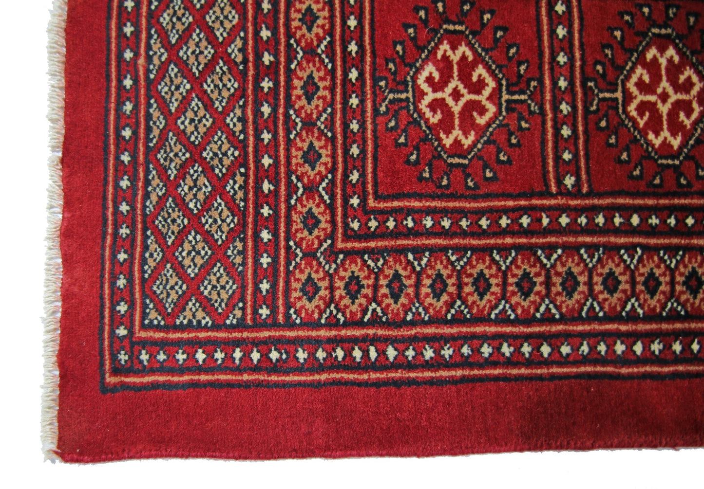 A vintage Pakistani Princess Bokhara rug featuring a geometric red pattern and fringed edges.