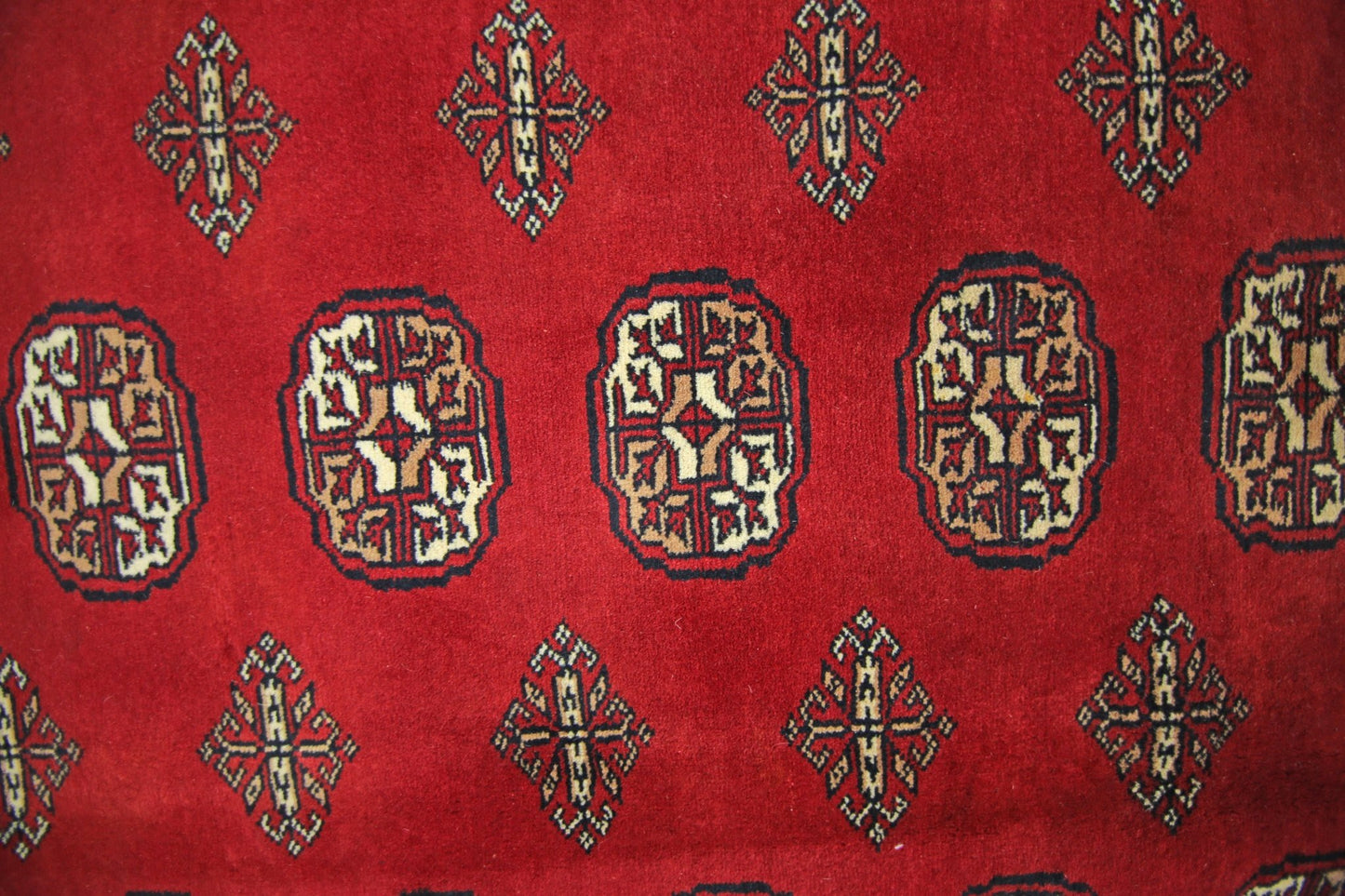 A vintage Pakistani Princess Bokhara rug featuring a repeating geometric pattern on a red background.