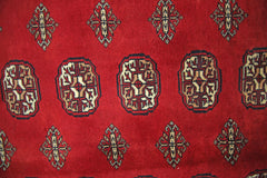A vintage Pakistani Princess Bokhara rug featuring a repeating geometric pattern on a red background.
