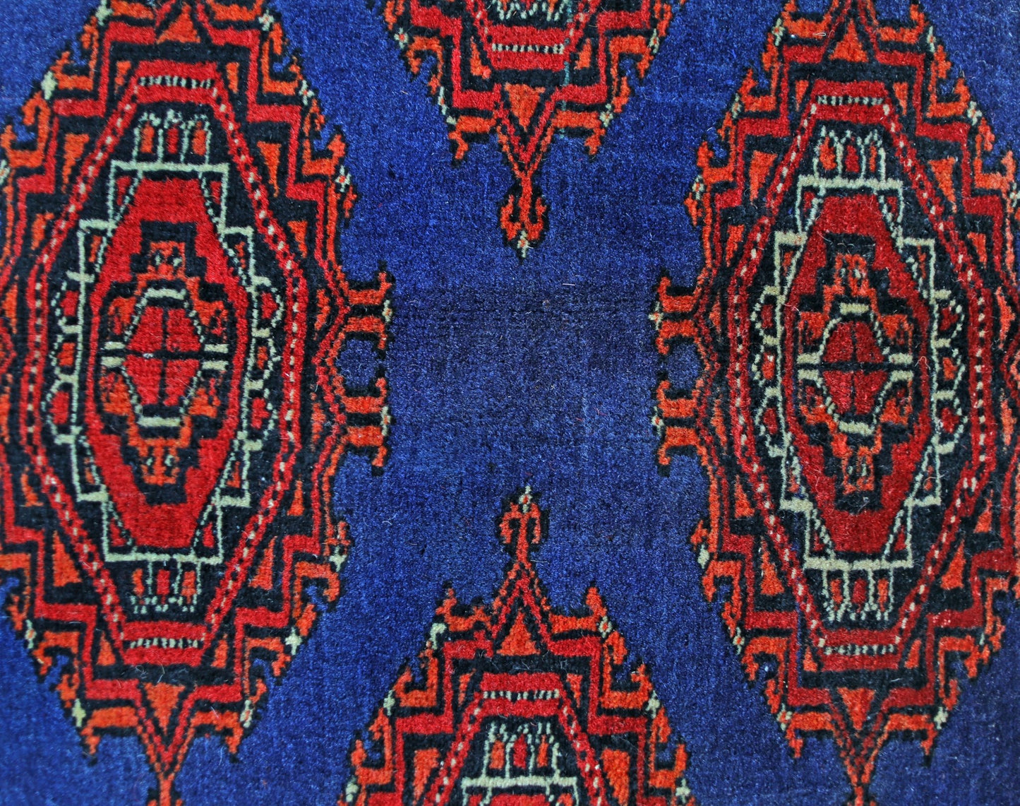 A vintage Pakistani Princess Bokhara rug featuring a geometric red pattern on a blue background.
