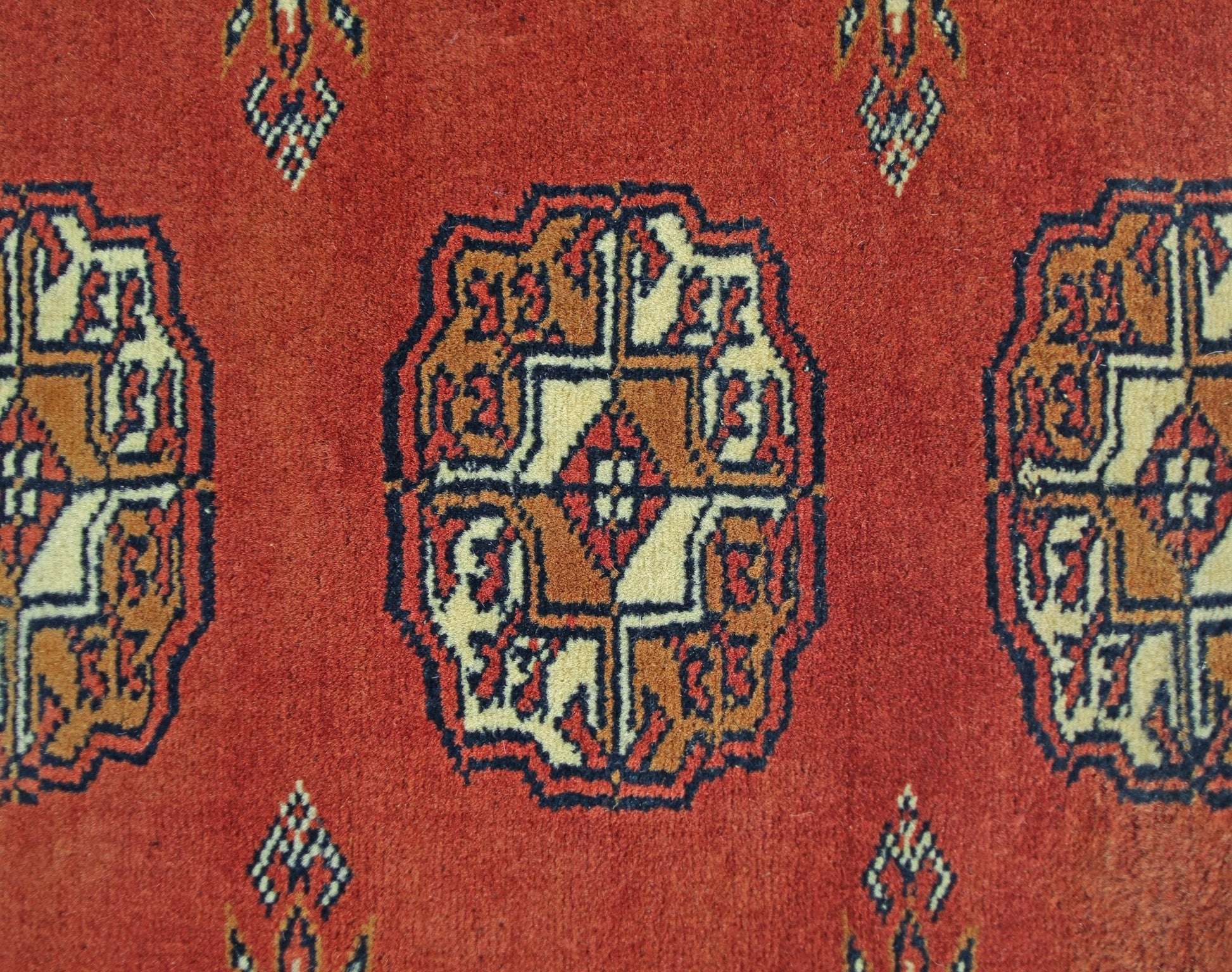 A vintage Pakistani runner rug featuring repeating geometric Bokhara motifs in red and tan wool.