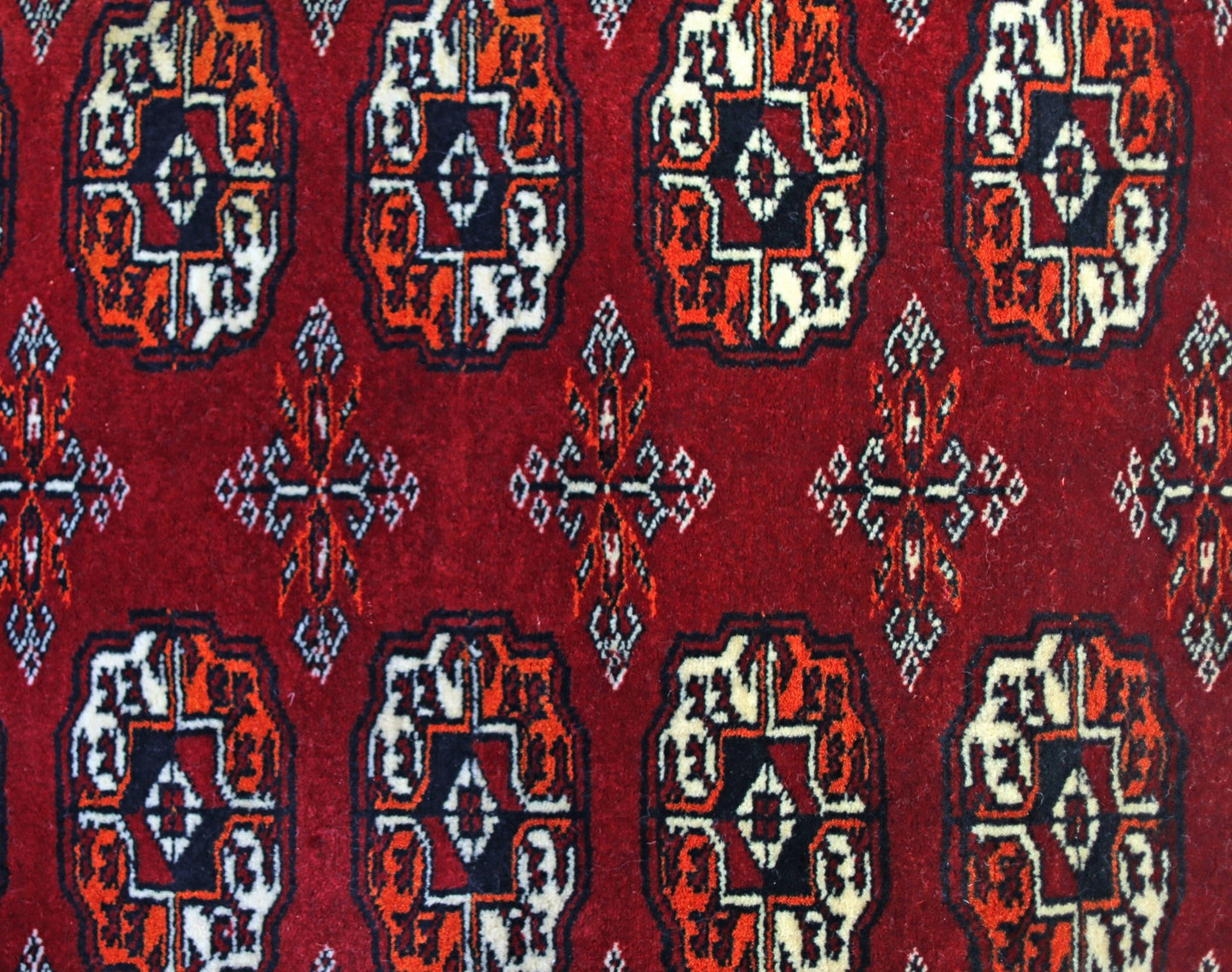 A vintage Pakistani runner rug featuring a repeating geometric Bokhara pattern in red, black, and white.
