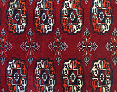 A vintage Pakistani runner rug featuring a repeating geometric Bokhara pattern in red, black, and white.