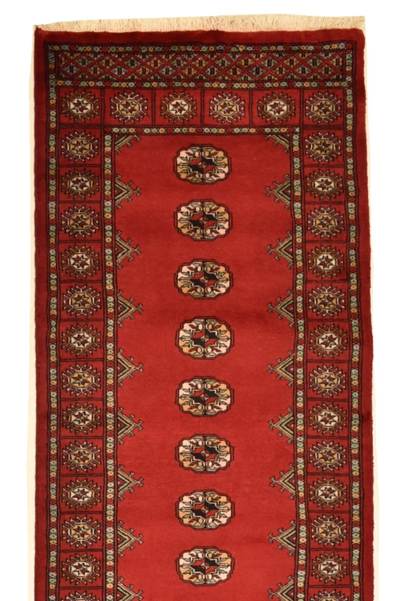 A handmade red wool runner rug featuring a repeating Princess Bokhara geometric pattern.
