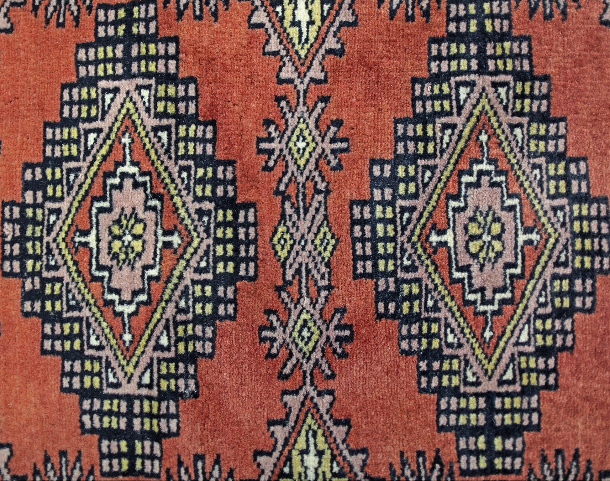 A vintage Pakistani runner featuring repeating geometric diamond motifs in red, black, and yellow.