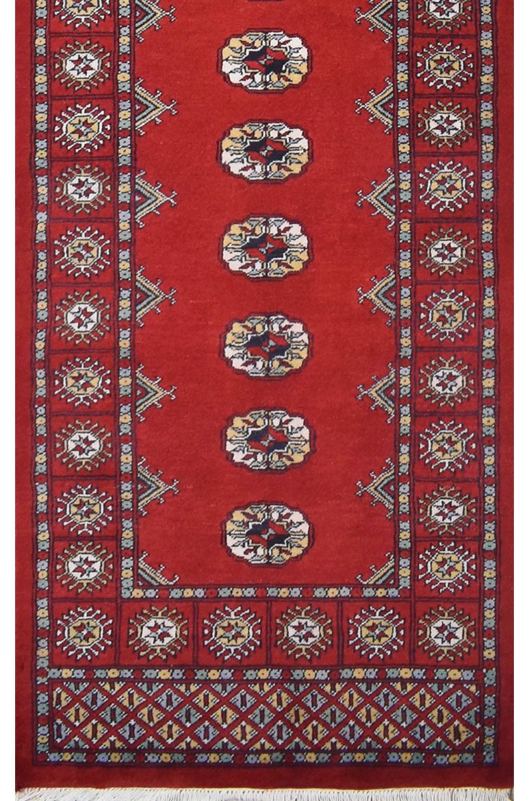 A handmade red wool runner rug featuring repeating geometric Bokhara motifs and a patterned border.