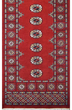A handmade red wool runner rug featuring repeating geometric Bokhara motifs and a patterned border.