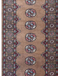 A handmade wool runner rug featuring a tan field with repeating geometric medallions and borders.