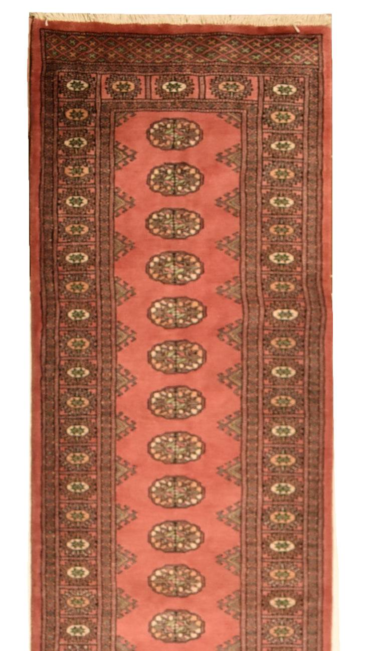 A handmade wool runner rug featuring a repeating Princess Bokhara pattern in shades of red.