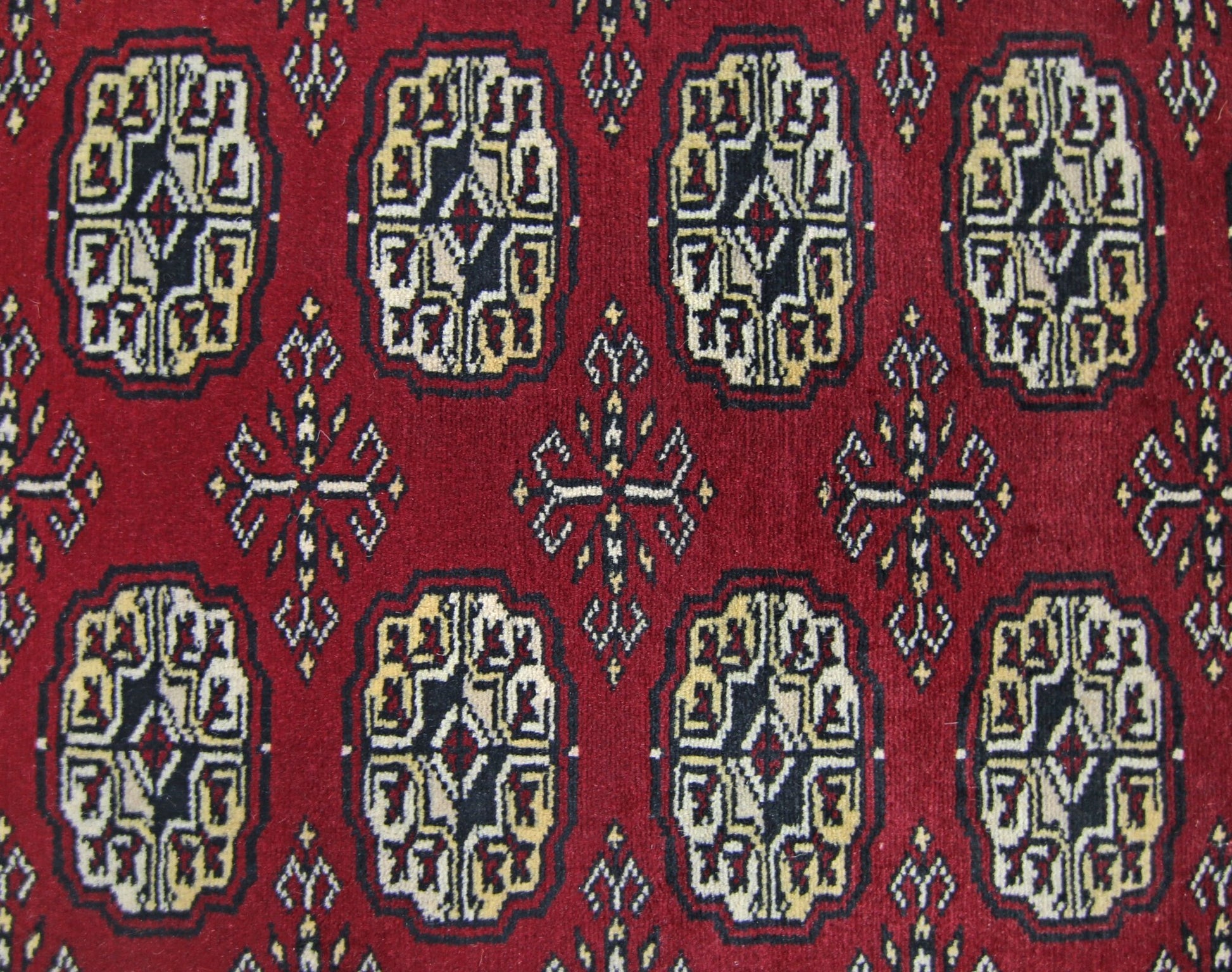 A vintage Pakistani runner rug featuring a repeating pattern of dark red octagonal guls and crosses.