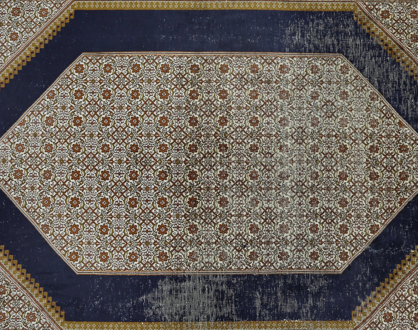 A vintage Kashmiri silk rug featuring a central floral lattice pattern on a dark blue background.