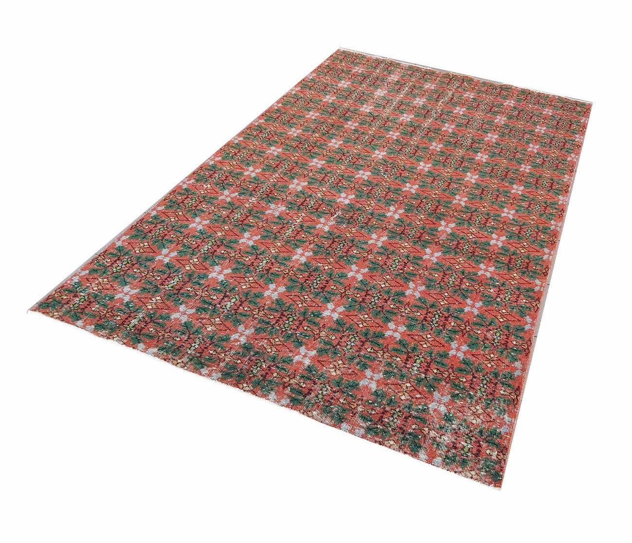 A rectangular vintage Turkish rug featuring a repeating geometric pattern in red and green tones.