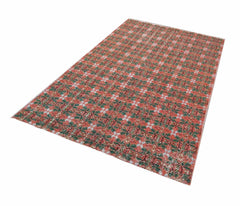 A rectangular vintage Turkish rug featuring a repeating geometric pattern in red and green tones.
