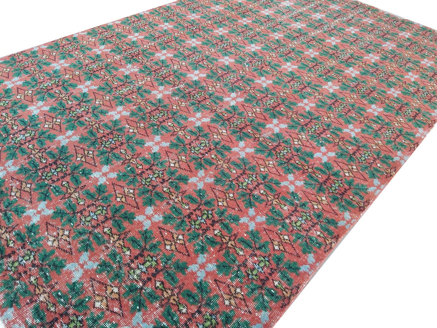 A vintage Turkish rug featuring a repeating geometric floral pattern in red, green, and blue.