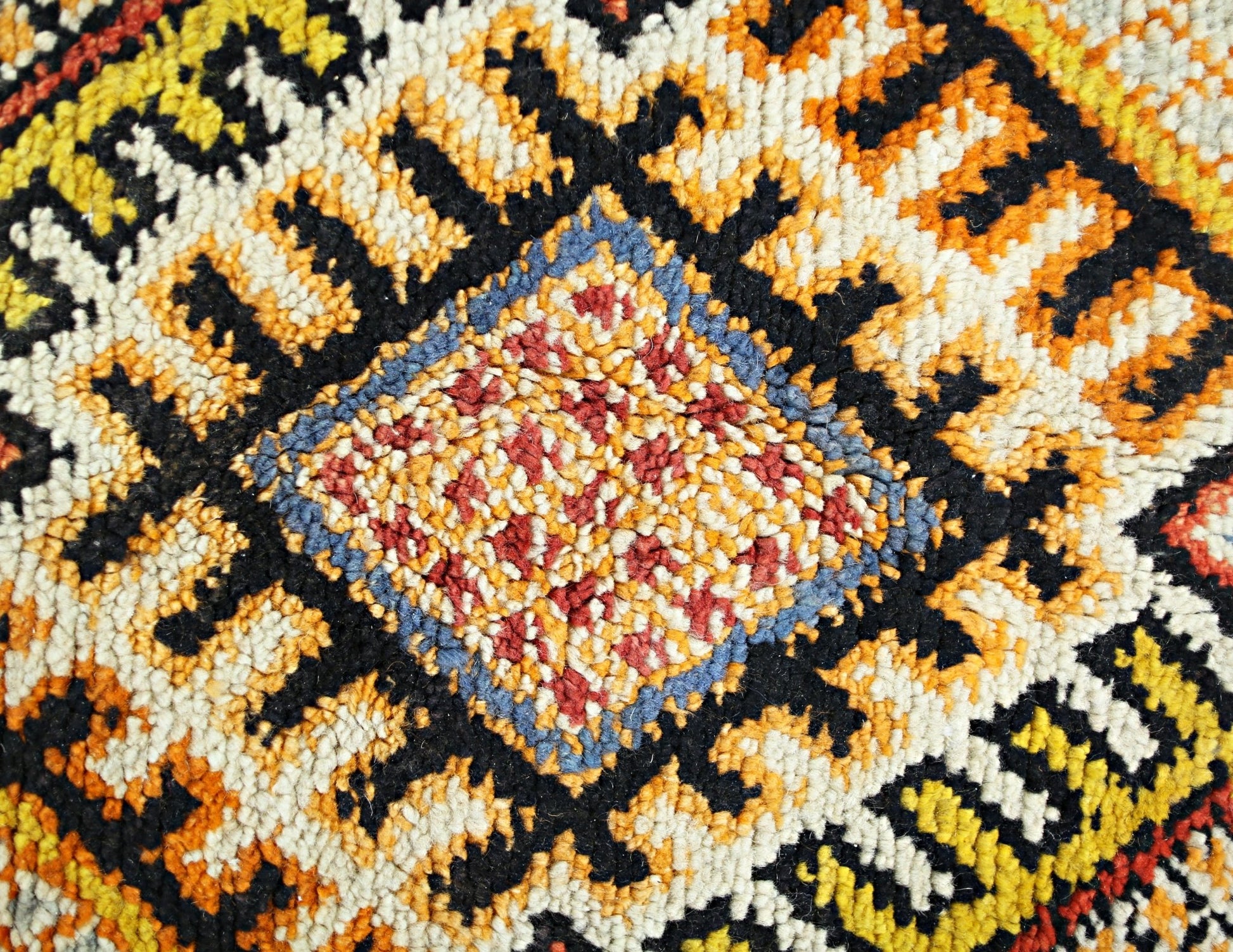 A close-up of a vintage Turkish rug featuring a central diamond motif in red, blue, and yellow.