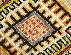 A close-up of a vintage Turkish rug featuring a central diamond motif in red, blue, and yellow.