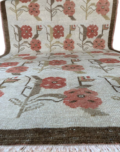 A vintage Turkish Oushak rug featuring a cream background with a repeating floral tulip pattern.