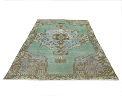 A vintage handmade Turkish rug featuring a central geometric medallion in blue and brown on a green field.