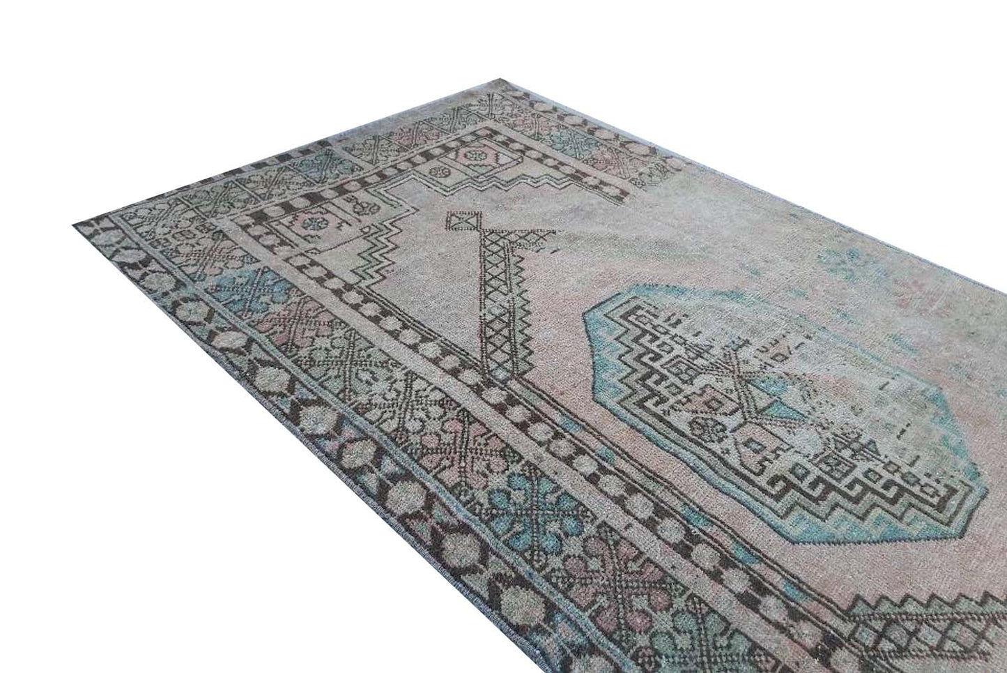 A vintage handmade Turkish wool rug featuring a faded geometric pattern in pink and blue tones.