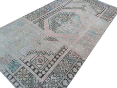 A vintage handmade Turkish wool rug featuring a faded geometric pattern in soft pink and blue tones.