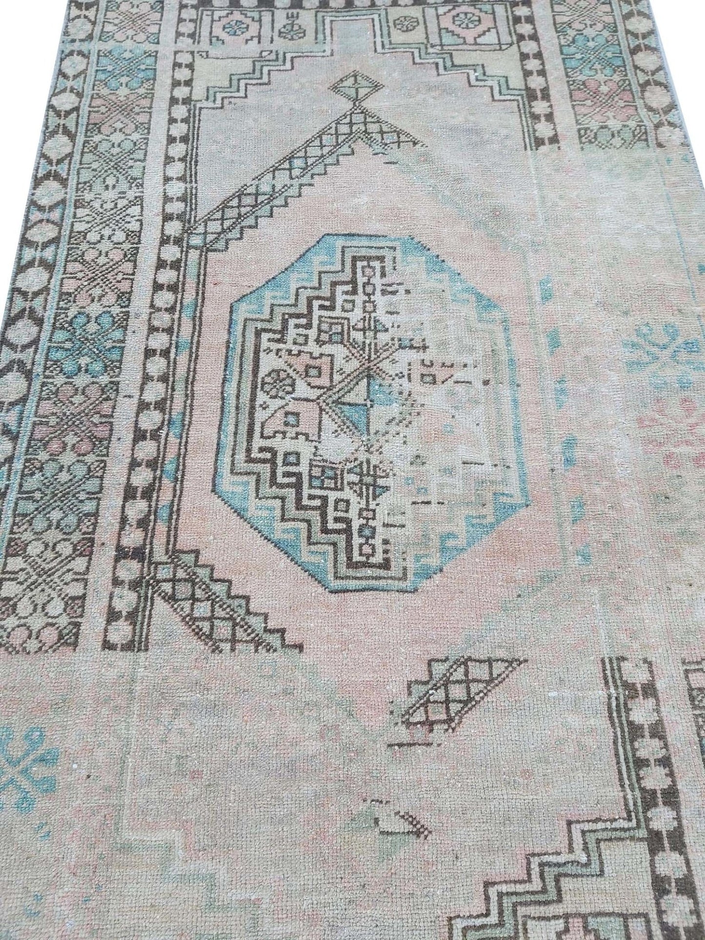 A vintage handmade Turkish wool rug featuring geometric patterns in faded pink and blue tones.