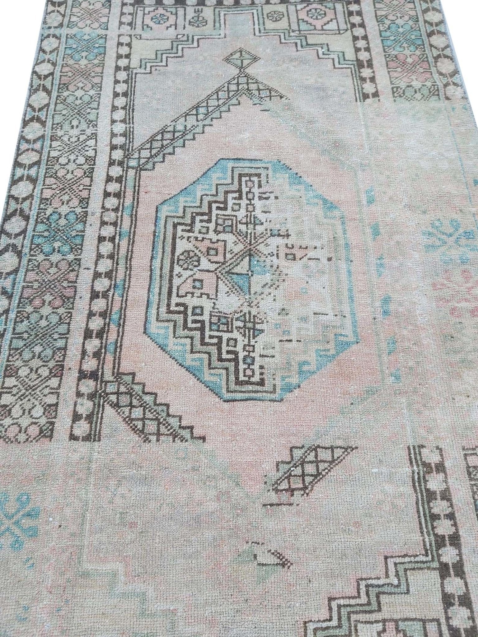 A vintage handmade Turkish wool rug featuring geometric patterns in faded pink and blue tones.