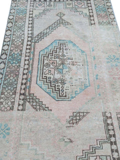 A vintage handmade Turkish wool rug featuring geometric patterns in faded pink and blue tones.