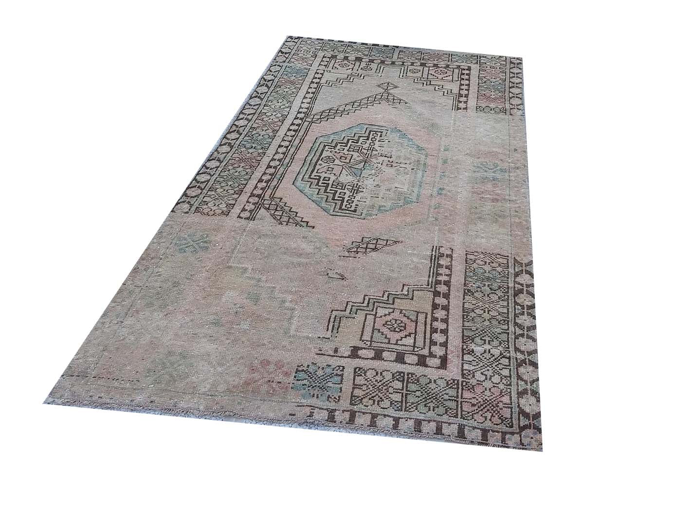 A vintage handmade Turkish wool rug featuring a faded geometric medallion on a muted pink field.