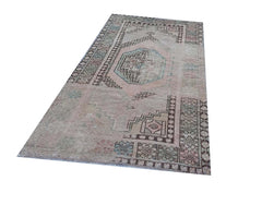 A vintage handmade Turkish wool rug featuring a faded geometric medallion on a muted pink field.