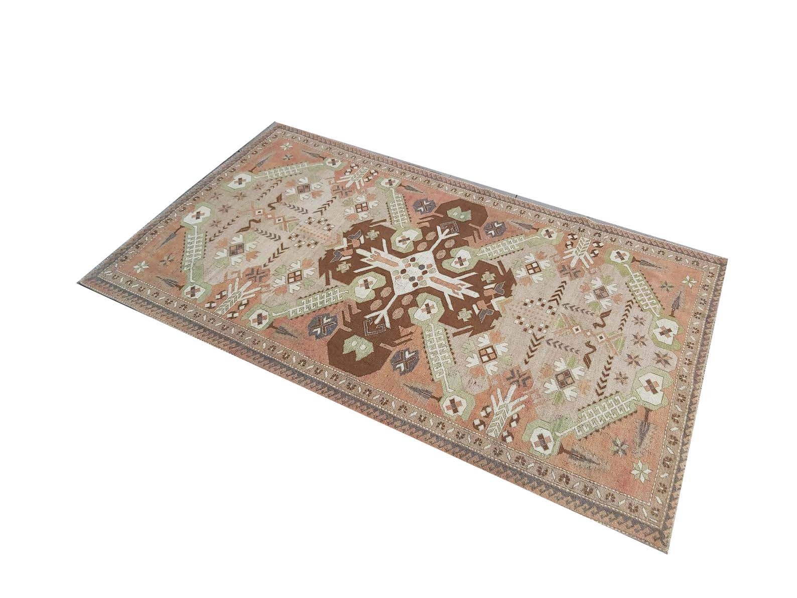 A vintage handmade Turkish rug featuring geometric patterns in shades of brown, green, and peach.