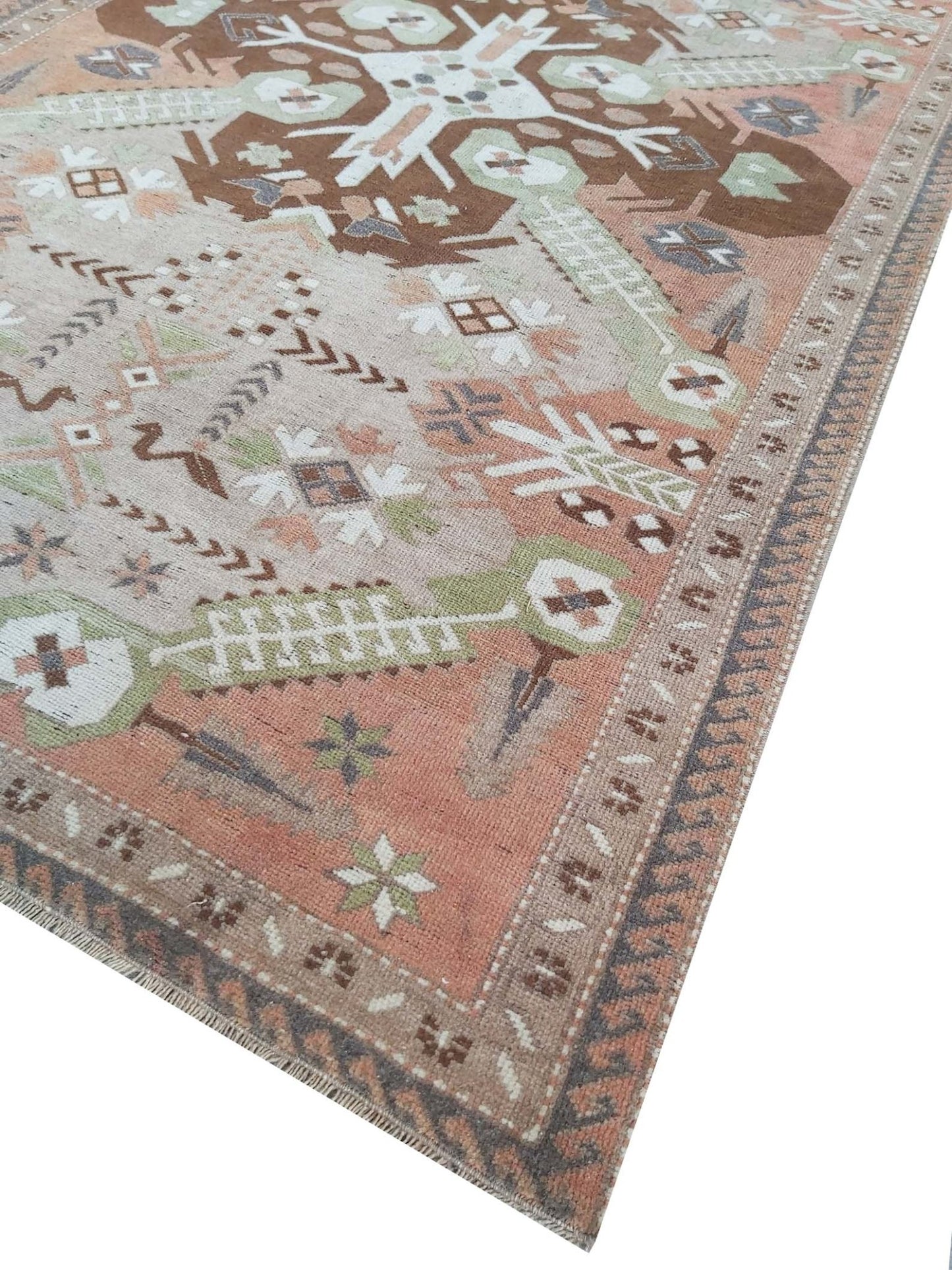 A vintage handmade Turkish rug featuring geometric patterns in shades of brown, green, and pink.
