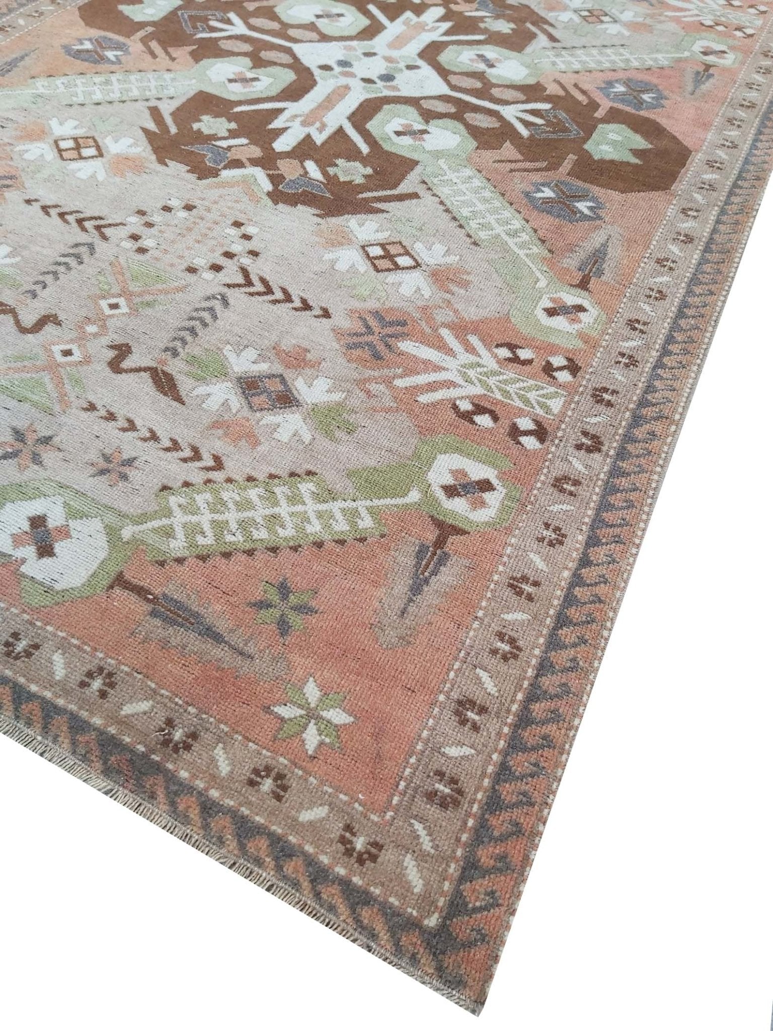 A vintage handmade Turkish rug featuring geometric patterns in shades of brown, green, and pink.