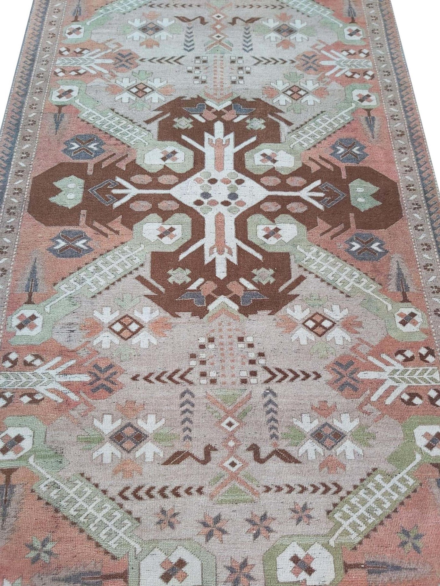 A vintage handmade Turkish wool rug featuring geometric patterns in brown, green, and peach tones.