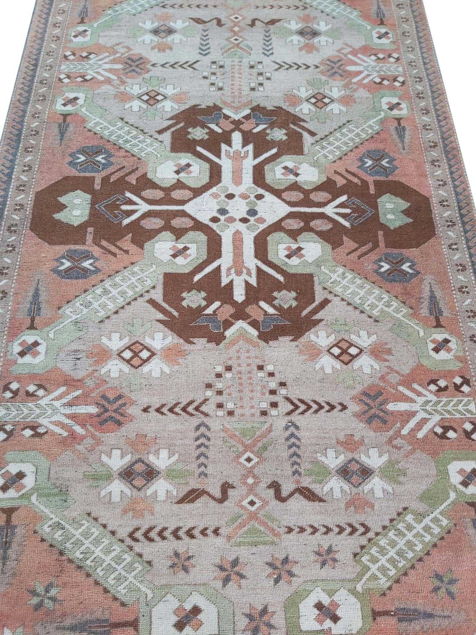 A vintage handmade Turkish wool rug featuring geometric patterns in brown, green, and peach tones.