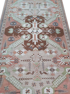 A vintage handmade Turkish wool rug featuring geometric patterns in brown, green, and peach tones.