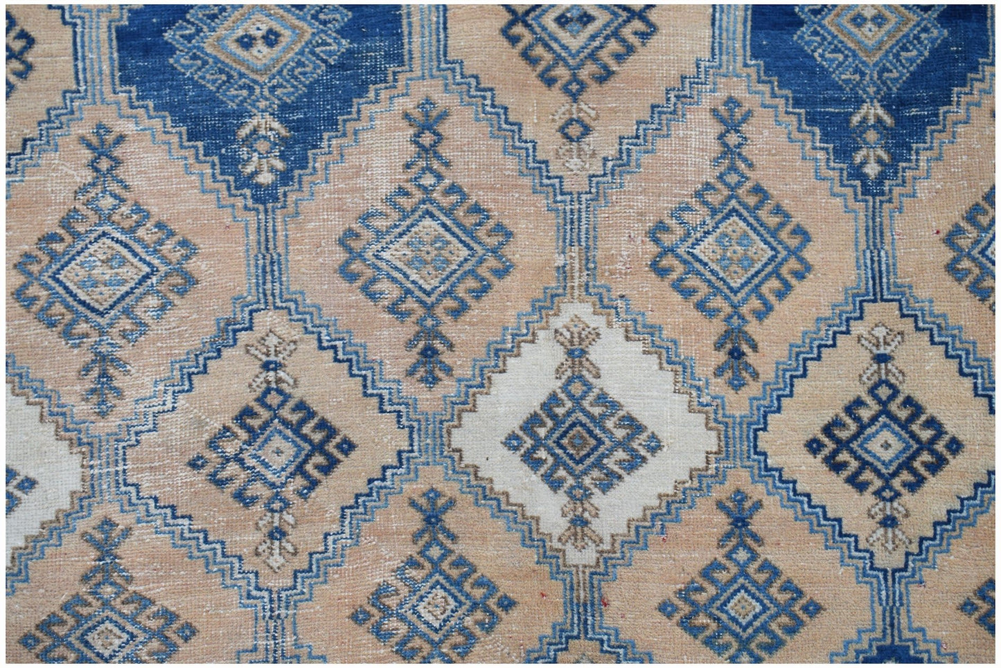 A vintage Persian rug featuring a geometric diamond pattern in shades of blue, cream, and tan.