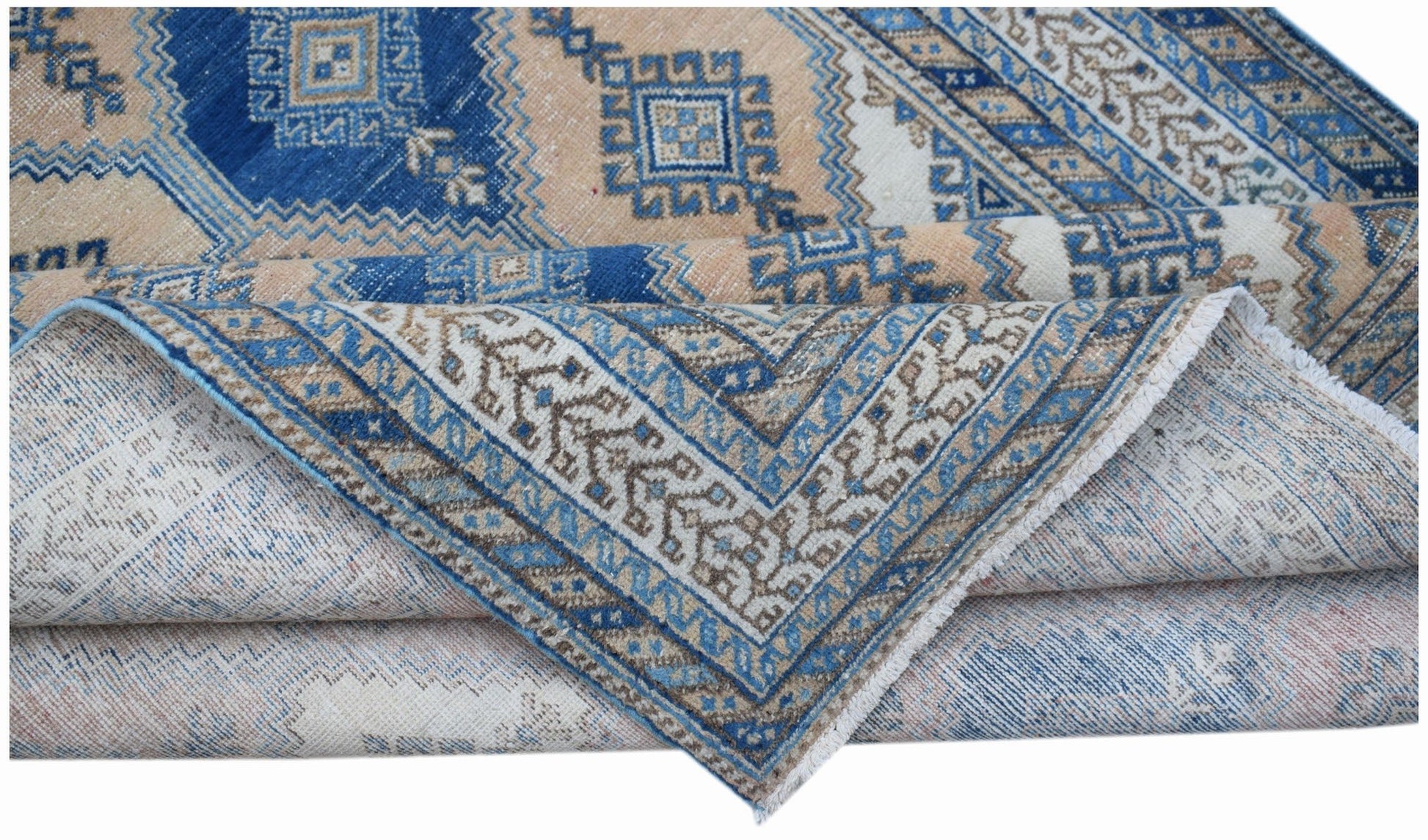 A folded vintage Persian rug featuring a traditional geometric pattern in blue and beige tones.