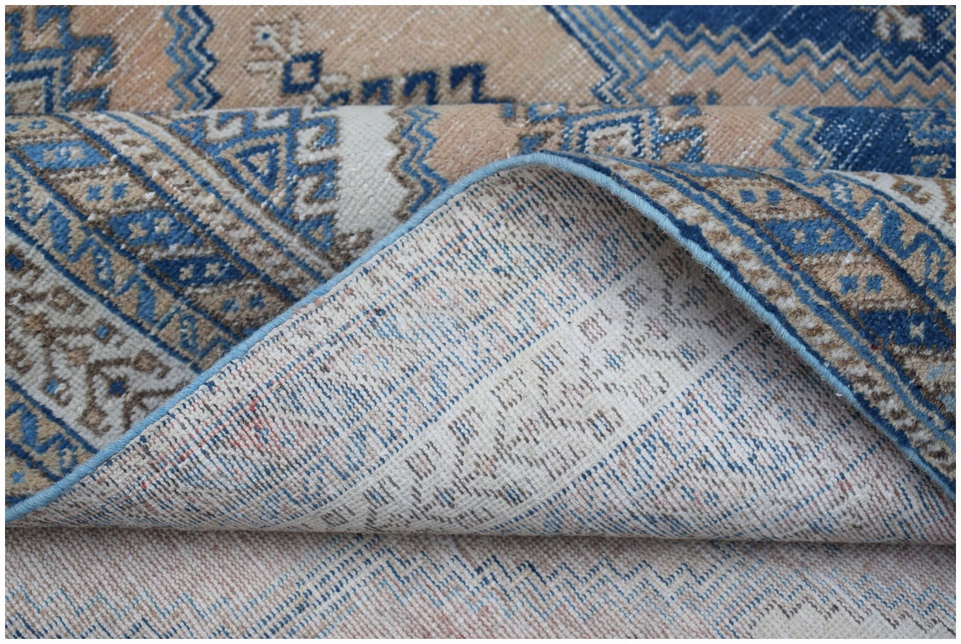 A folded vintage Persian rug featuring a traditional blue and beige geometric pattern.
